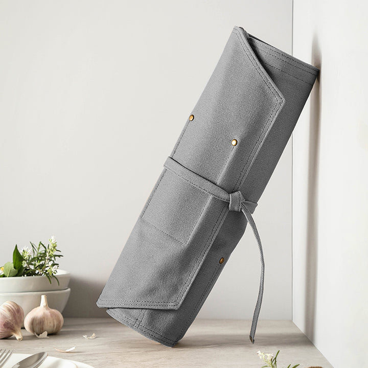 Opgerolde grijze canvas messentas met gouden details tegen muur
